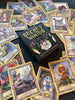 The Secret Woods deck by Schiffer Publishing, Ltd. features illustrated intuition cards with whimsical forest creatures and includes a black and gold guidebook, all displayed on a dark surface.