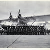 A large group of uniformed personnel poses before a twin-engine seaplane, reflecting US Navy history—an image featured in King's Navy by Schiffer Publishing, Ltd. The group gathers on the tarmac beneath the plane's wings and propellers.