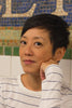 A person with short dark hair wearing a white shirt with blue stripes sits before a mosaic wall inspired by New York MTA Arts & Design, evoking the style featured in "Museum in Transit" by Schiffer Publishing, Ltd.