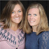 Two women with shoulder-length blonde hair and blue eyes smile together, wearing patterns inspired by Baby Knits from Norway by Schiffer Publishing, Ltd.; one has on a pink patterned sweater, the other a blue lace-sleeved top, both set against a dark background.