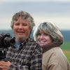 A man holding a camera on a tripod stands next to a smiling woman against the background of the Vineyards of Napa Valley book.