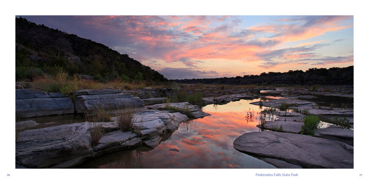 A scenic Texas sunset from Texas Hill Country features pink and orange clouds reflecting in the calm water of Pedernales Falls State Park, flowing past rocky river banks.