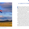 An Icelandic flag from the Iceland book by Schiffer Publishing, Ltd. waves on a flagpole against a cloudy sky above a landscape of dramatic volcanoes.