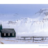 A small black wooden church from the Schiffer Publishing, Ltd. Iceland book sits in a snow-covered Icelandic landscape in front of large, frost-dusted mountains.