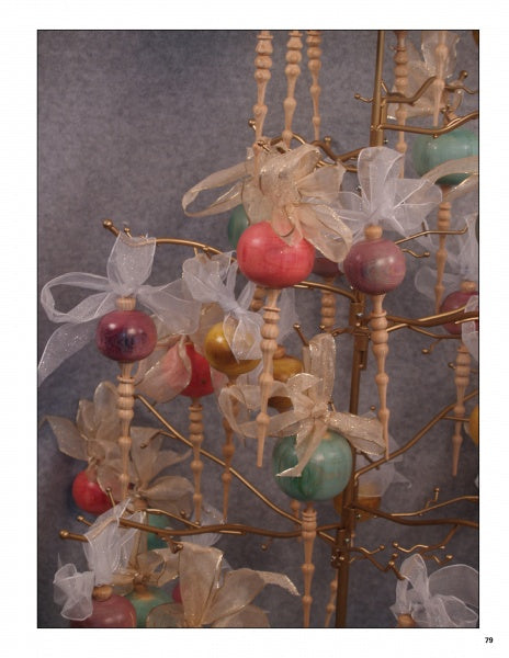 A decorative display for "Wood Turning, from Tree to Table" by Schiffer Publishing, Ltd. features spindles and colorful ornaments with gold and white ribbon bows on a gold stand, set against a gray background.