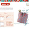 A floral tote with red handles sits on the ground, filled with fabric and a baguette. Nearby is "The Little Guide to Mastering Your Sewing Machine" by Schiffer Publishing, Ltd., with sewing instructions and supply lists for making the bag.