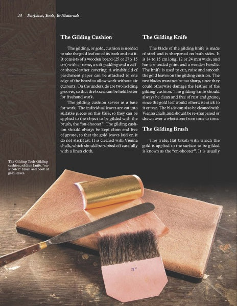 A copy of "GOLD" by Schiffer Publishing, Ltd. rests on a soft, light brown surface with a gilding brush, gold knife, and gold leaf, illustrating essential tools and techniques for gold crafting and gilding.