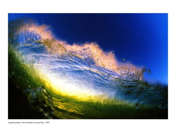 A vibrant underwater view of a breaking wave illuminated by sunlight in yellow, blue, and gold hues beneath a deep blue sky. Surfing photography by Jim Russi. Text at the bottom reads: Flying Through the Clouds, Schiffer Publishing, Ltd.