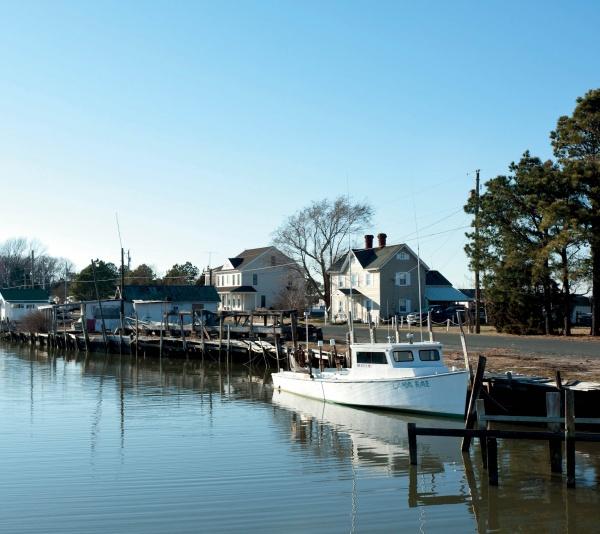 The book "Eastern Shore Perspectives" by Schiffer Publishing, Ltd. captures a white fishing boat docked on calm waters beside wooden piers, with houses and trees along Maryland’s Eastern Shore on a clear blue day.