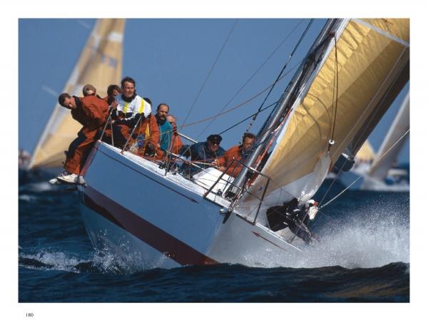 A group sails a racing yacht with yellow sails, leaning over the edge as it cuts through the water in this striking photo from "Sailing Fascination" by Schiffer Publishing, Ltd. Other boats are seen in the background on a sunny day.