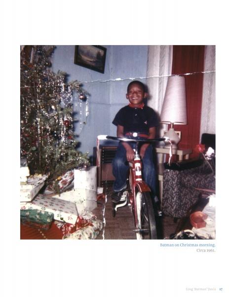 A smiling child sits on a red bike by wrapped presents and a Christmas tree in a cozy room. The vintage photo has a worn look, like the Original Gangster era. Product: Greg Batman Davis by Schiffer Publishing, Ltd.