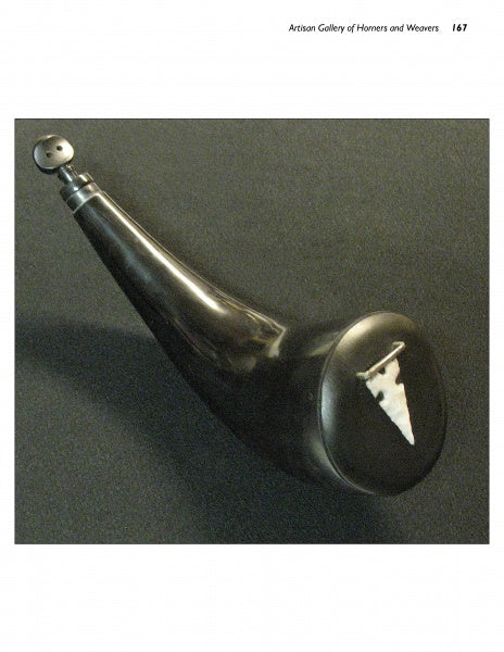 The Powder Horns by Schiffer Publishing, Ltd. features a smooth, curved black body with a round stopper and an inlaid arrowhead shape on the wide end—a fine example of powder horn making—displayed on a dark surface.