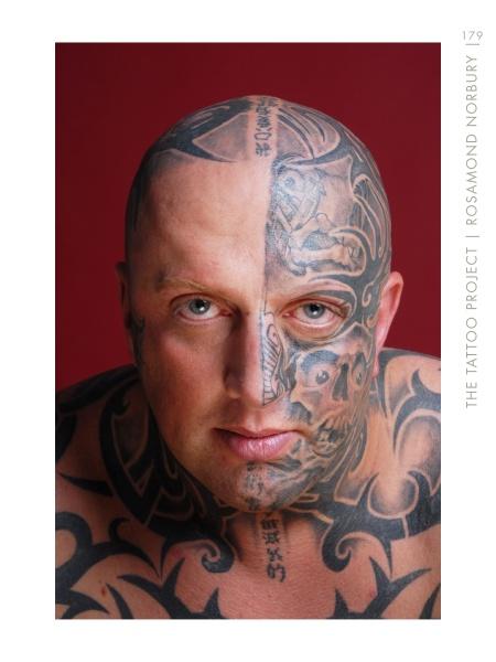 A bald man with intricate black tattoos on his face and upper body stares at the camera, set against a deep red background. Featured in "The Tattoo Project" by Schiffer Publishing, Ltd., this portrait showcases bold tattoo artistry.