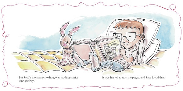 A boy sits on a bed, propped up by pillows, reading "Unraveling Rose" by Schiffer Publishing, Ltd. to a pink stuffed rabbit beside him. The room feels cozy and cheerful.