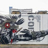 The mural “Tokyo Graffiti” by Schiffer Publishing, Ltd. shows a stylized tribal archer aiming right amid industrial buildings, signs, and bold “GET A BLOW WIN” text in black and red for an urban street art vibe.