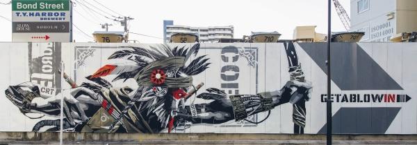 The mural “Tokyo Graffiti” by Schiffer Publishing, Ltd. shows a stylized tribal archer aiming right amid industrial buildings, signs, and bold “GET A BLOW WIN” text in black and red for an urban street art vibe.