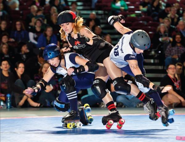 Three modern roller derby players in helmets and pads clash and fall on a rink during intense action in "No Mercy" by Schiffer Publishing, Ltd., as a crowd watches this thrilling contact sport.