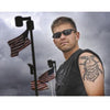 A man stands outdoors in sunglasses and a sleeveless shirt, revealing a large military tattoo on his upper arm, as three American flags wave behind him; featured on the cover of "War Paint" by Schiffer Publishing, Ltd.
