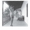 A black and white 1950s-style photo from "Femmes Fatales of the 1950s" by Schiffer Publishing, Ltd. shows a woman in lingerie and sandals posing on a columned balcony with crossed legs, as palm trees and a bench appear in the background.